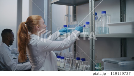 Female chemist takes test tubes from shelf with lab glassware 119129727
