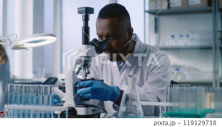 African American scientist looks under microscope, studies samples of new drug 119129738