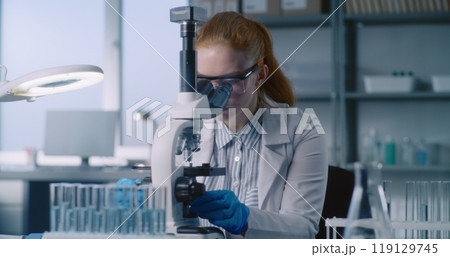 Female biochemist takes liquid from test tube, looks under microscope 119129745