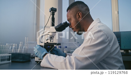 Medical science lab: African American male microbiologist looking under microscope 119129768