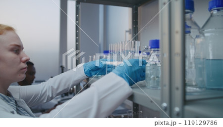 Medical science lab: Female chemist in white coat takes test tubes from the shelf 119129786