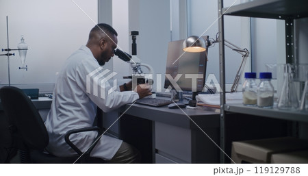 African American microbiologist looks under microscope, does analysis African American microbiologist looks under microscope, does analysis 119129788