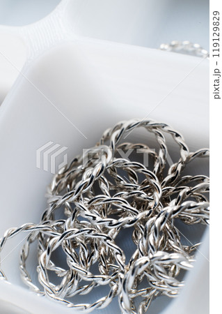 Close-up macro shot of small silver jewelry pieces lying in a white mesh box. DIY jewelry Close-up macro shot of small silver jewelry pieces lying in a white mesh box. DIY jewelry 119129829