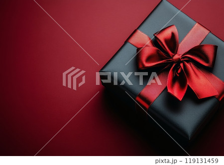 A beautifully wrapped black gift box with a red ribbon on a textured red and black background 119131459