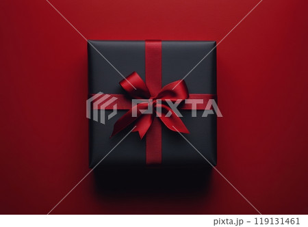 A beautifully wrapped black gift box with a red ribbon on a vibrant red backdrop 119131461