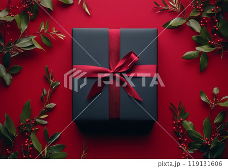 A beautifully wrapped black gift box with a red ribbon on a vibrant red backdrop 119131606