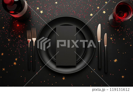 Elegant dinner setting with red wine, black plate, and golden cutlery on a dark table 119131612