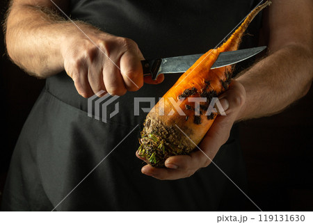 A cook tries to cut an orange beetroot with a knife. Low key concept of cooking a vegetable diet dish in the kitchen A cook tries to cut an orange beetroot with a knife. Low key concept of cooking a vegetable diet dish in the kitchen 119131630