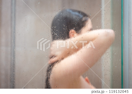 Side view of naked young woman taking a shower in modern grey bathroom. Body is in blur. Daily hygiene routine and hair care Side view of naked young woman taking a shower in modern grey bathroom. Body is in blur. Daily hygiene routine and hair care 119132045