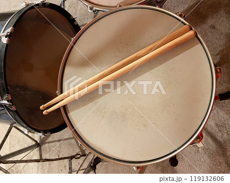 Pair of wooden drumsticks rests on a snare drum, inviting rhythm and energy. Musical experience waiting to unfold in this intimate setting 119132606