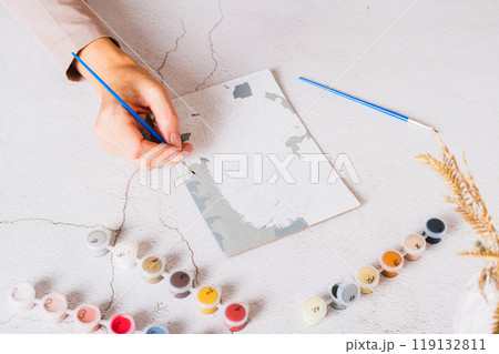 A woman's hand paints a picture by numbers on a table with a brush A woman's hand paints a picture by numbers on a table with a brush 119132811
