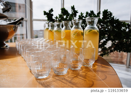 Fresh lemonades in glass jugs and empty glasses arranged on a table, summer events or catering Fresh lemonades in glass jugs and empty glasses arranged on a table, summer events or catering 119133659