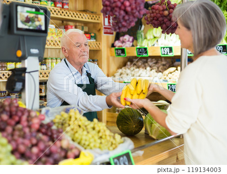 Male grocery store worker handing bananas to customer after payment at checkout closeup 119134003