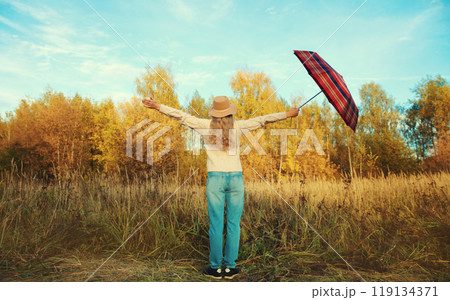 Back view, happy woman in autumn park raising hands up with umbrella, enjoying warm sunny weather Back view, happy woman in autumn park raising hands up with umbrella, enjoying warm sunny weather 119134371