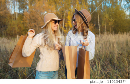 Fashionable happy young two women friends with shopping bags, stylish smiling girlfriends in park 119134374