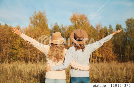 Back view, happy two women friends enjoying in autumn park, stylish girlfriends together outdoors 119134376