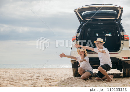 Asian family of three is playing on the beach on back car, with a young girl running towards car. Father and mother open their arms to welcome their daughter running towards them, summer trip concept Asian family of three is playing on the beach on back car, with a young girl running towards car. Father and mother open their arms to welcome their daughter running towards them, summer trip concept 119135328