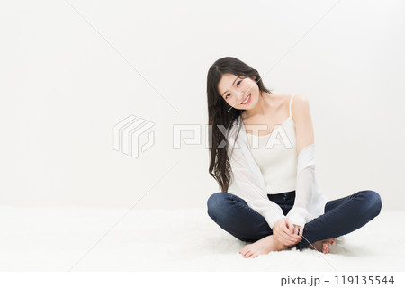 スキニージーンズ・ジーパン・デニムパンツをはいて胡座をかいて座る若い女性 119135544