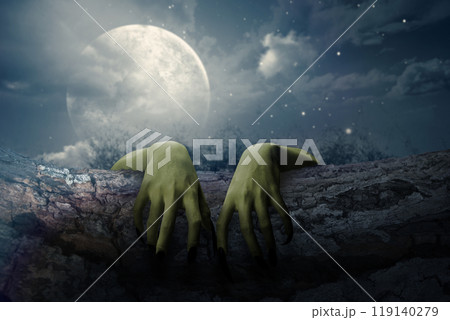 Two witch hands reaching out from a wooden log with full moon background. Scene is scary and creepy. The hand appearing to be a evil, satan, zombie or a monster hand 119140279