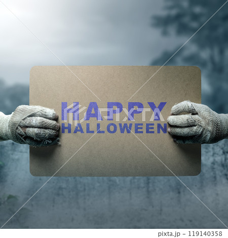 Mummy hands have dirty bandages on them. Mummy, devil, evil, satan, or zombie hands holding a piece of brown paper with a Happy Halloween sign Mummy hands have dirty bandages on them. Mummy, devil, evil, satan, or zombie hands holding a piece of brown paper with a Happy Halloween sign 119140358