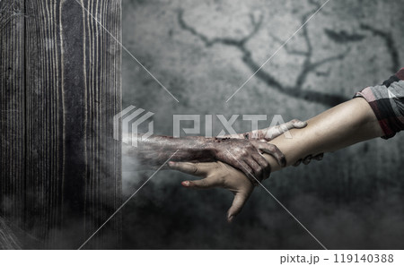 A zombie hand with a bloody wound grabs a human hand in dark room. Scene has dark and scary. Zombie, devil, evil, satan, or monster hands 119140388