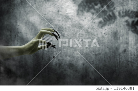 Witches hand with long nail claw is reaching out. The color is green. Evil, zombie, or monster hand is shown in a dark room 119140391
