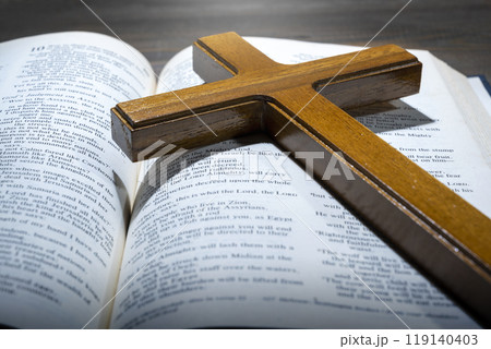 Wooden religion cross and opened blue book of Holy Bible. It is laying on a wooden table. Religious christian holiday. Symbol of faith in God, Christianity Feast Wooden religion cross and opened blue book of Holy Bible. It is laying on a wooden table. Religious christian holiday. Symbol of faith in God, Christianity Feast 119140403