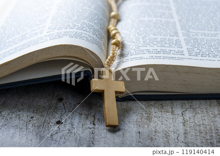 Wooden religion cross on rosary beads and opened blue book of Holy Bible. It is laying on a wooden table. Religious christian holiday. Symbol of faith in God, Christianity Feast Wooden religion cross on rosary beads and opened blue book of Holy Bible. It is laying on a wooden table. Religious christian holiday. Symbol of faith in God, Christianity Feast 119140414