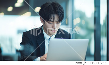 スーツを着た若い男性がモダンなオフィスでノートパソコンを使って作業している 119141266