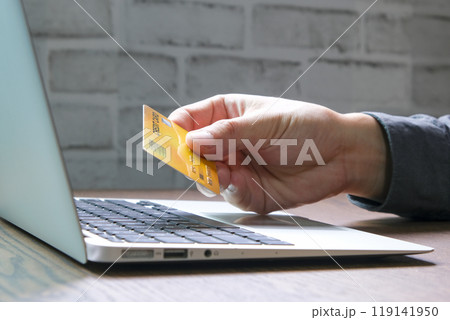Young man sat in the living room on sofa , using his laptop computer and holding credit card her online To buy product in the internet 119141950