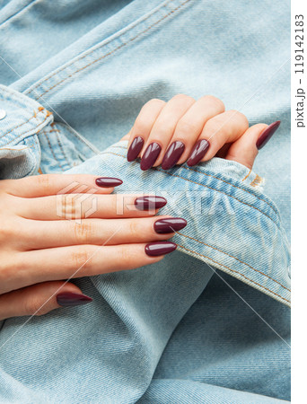 Elegant hands with polished burgundy nails resting on a denim jacket sleeve Elegant hands with polished burgundy nails resting on a denim jacket sleeve 119142183