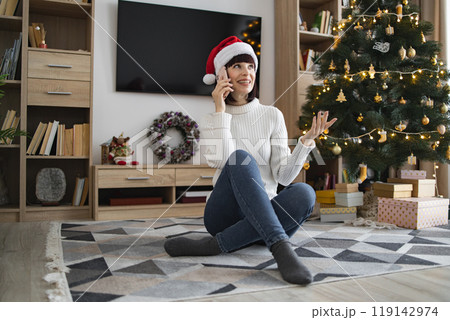 Woman enjoying holiday conversation by Christmas tree at home 119142974