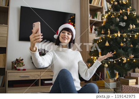 Young woman enjoys video call by Christmas tree at home 119142975