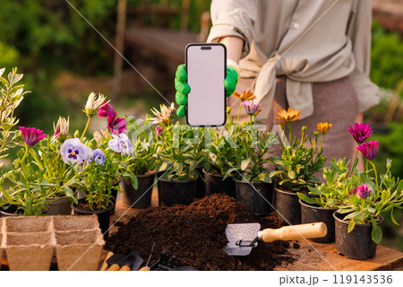 gardener using mobile app in phone for proper planting of flower plants in garden, gardening concept 119143536
