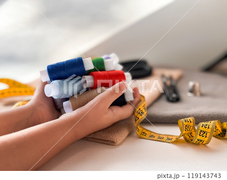 Childs hands holding colorful threads with sewing supplies on a creative workspace Childs hands holding colorful threads with sewing supplies on a creative workspace 119143743