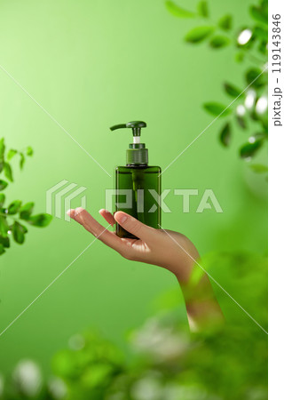 Natural product advertising image template showcases a mockup of a dark green pump bottle placed on the model's palm reaching out to the center of the image with a cool background of lush green trees. Natural product advertising image template showcases a mockup of a dark green pump bottle placed on the model's palm reaching out to the center of the image with a cool background of lush green trees. 119143846
