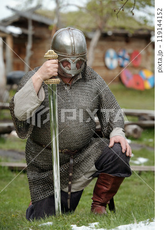 Kneeling Medieval Warrior Holding Sword in Battle Armor Kneeling Medieval Warrior Holding Sword in Battle Armor 119144152