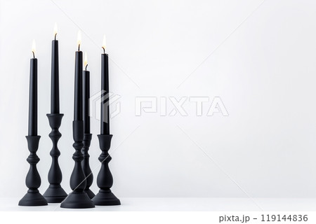 Black candles in stylish holders on a plain white background. Minimalistic display for home Halloween decor concepts Black candles in stylish holders on a plain white background. Minimalistic display for home Halloween decor concepts 119144836