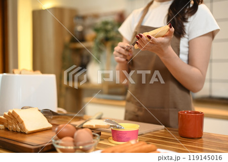 Young woman spreading butter on bread with a cutlery knife Young woman spreading butter on bread with a cutlery knife 119145016