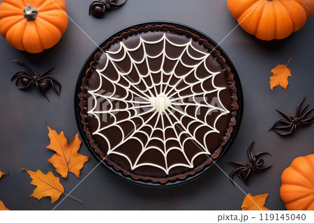 Chocolate tart with spider web design and spider decoration on black background. Concept of Halloween dessert Chocolate tart with spider web design and spider decoration on black background. Concept of Halloween dessert 119145040