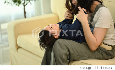 Joyful mother playing with laughing baby boy lying on her legs. Family, tenderness and parenthood concept Joyful mother playing with laughing baby boy lying on her legs. Family, tenderness and parenthood concept 119145083