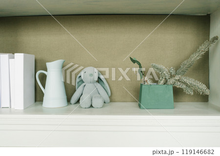 White shelf with a rabbit stuffed animal and a green vase 119146682