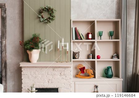 Beige fireplace mantel with christmas wreath and wooden rocking horse in living room 119146684