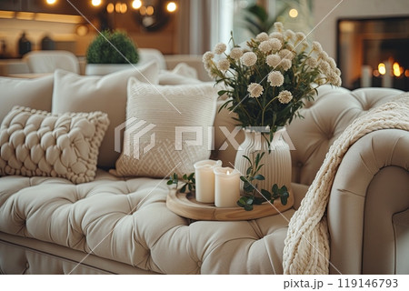 Beige couch with a vase of flowers and candles on a tray. Scene is warm and inviting 119146793
