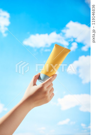 A mockup yellow cream tube is being held by a female model against a clear blue sky with white clouds drifting by. Minimalist image used for advertisements of skincare products. A mockup yellow cream tube is being held by a female model against a clear blue sky with white clouds drifting by. Minimalist image used for advertisements of skincare products. 119146836