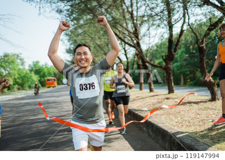 marathon runner crossing finish line with hands up gesture 119147994