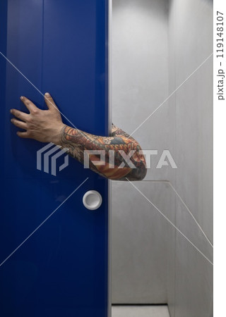 An intriguing arm emerges from a blue door in a contemporary space, captivating viewers 119148107
