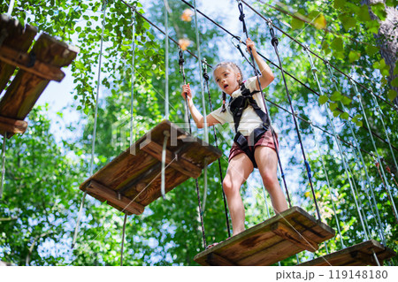 Young girl participating in outdoor adventure park, navigating through a rope obstacle course Young girl participating in outdoor adventure park, navigating through a rope obstacle course 119148180