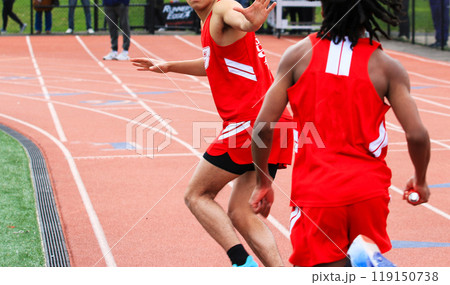 Runners exchanging the baton during a track relay race outdoors 119150738