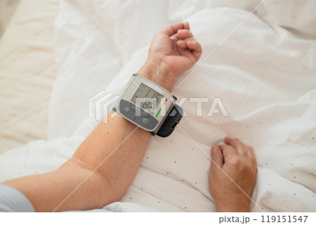 Close up of woman checks her blood pressure, a tonometer is worn on her wrist in a bed. Medical device for measuring blood pressure and heart rate used at hand wrist 119151547